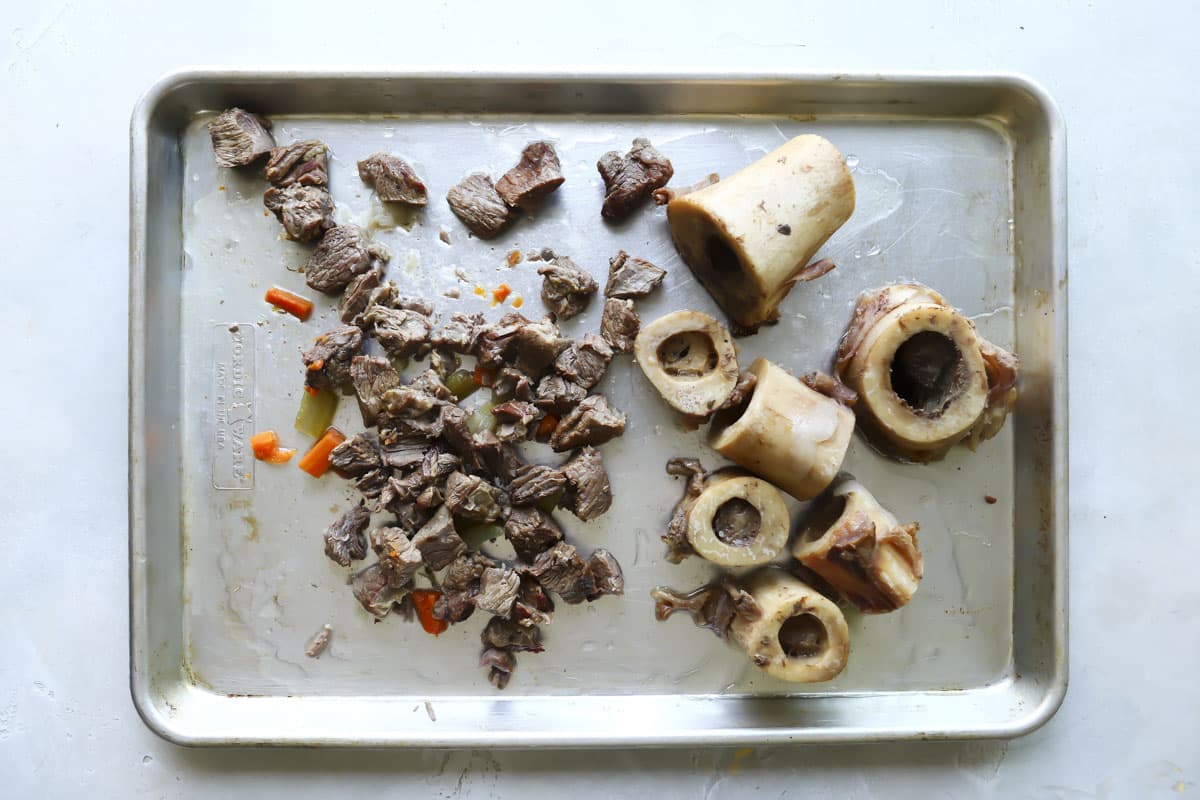 Roasted marrow bones and shredded beef on a baking sheet.