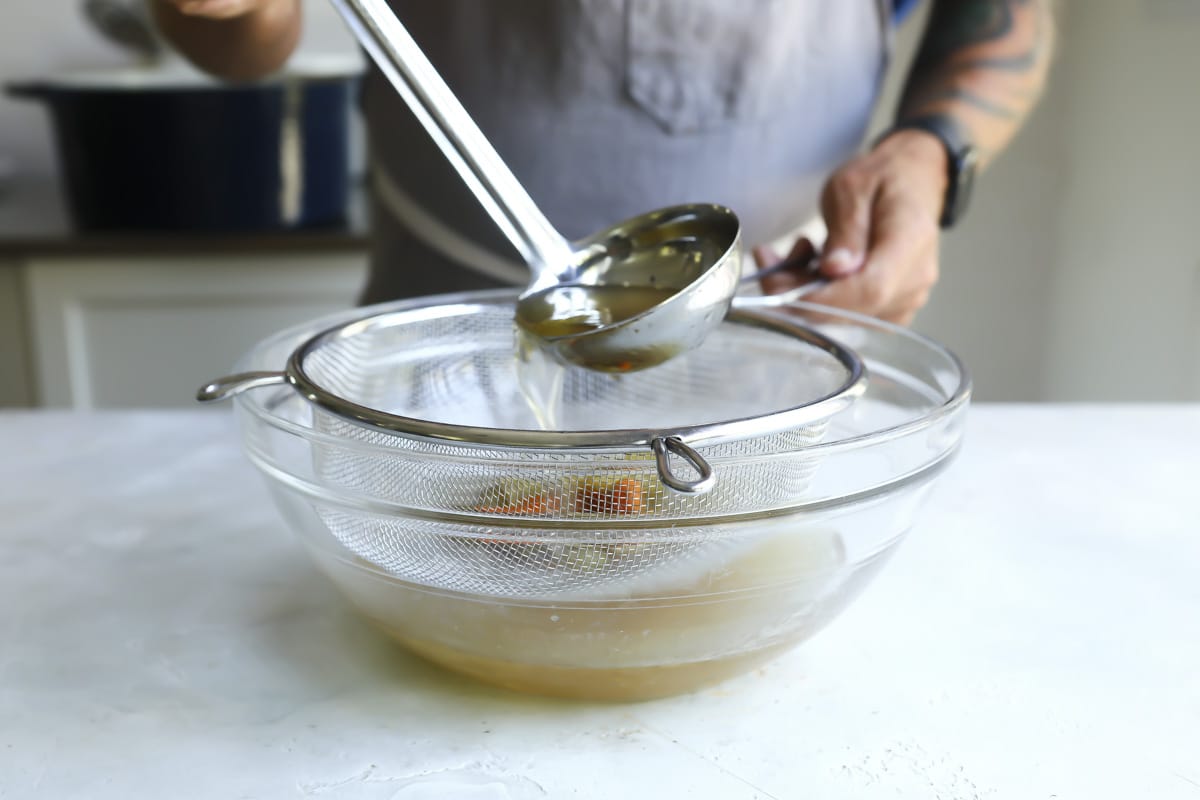 Straining beef broth through a fine mesh strainer.