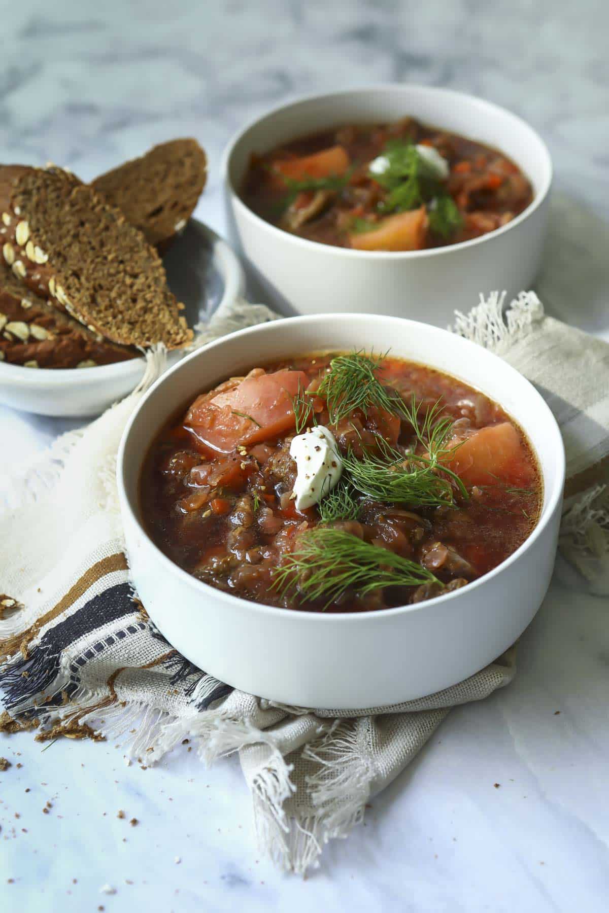 2 bowls of borscht soup with brown bread nearby.