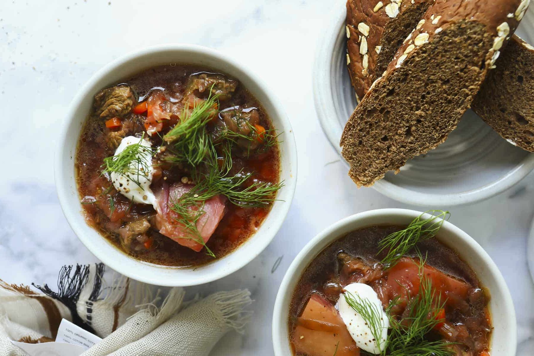 2 bowls of borscht soup with brown bread nearby.