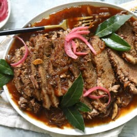 Braised beef brisket slices on a plate with red onions.