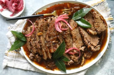 Braised beef brisket slices on a plate with red onions.