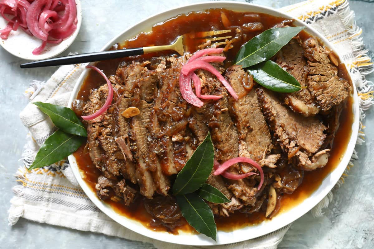 Braised beef brisket slices on a plate with red onions.