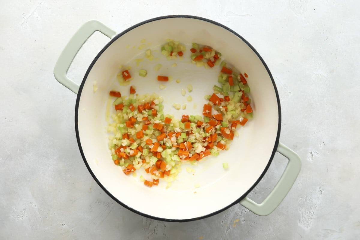 Cooking carrots, celery, and onion in the bottom of a pot.