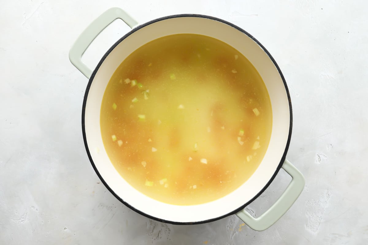 Adding broth to softened vegetables to make soup.