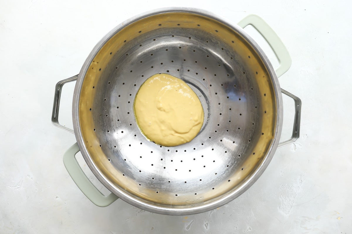 Pressing batter through a colander into soup for dumpling soup.