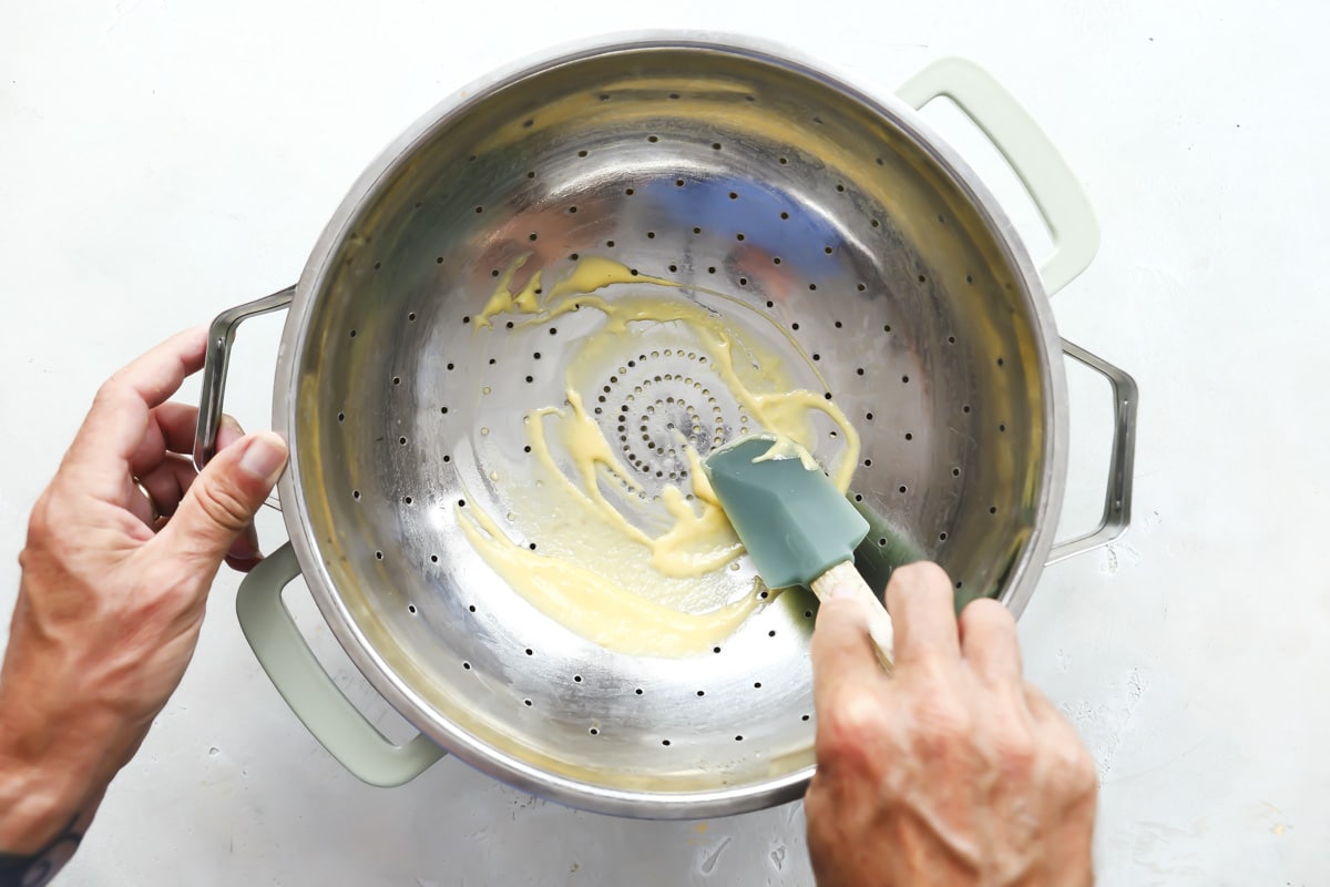 Pressing batter through a colander into soup for dumpling soup.