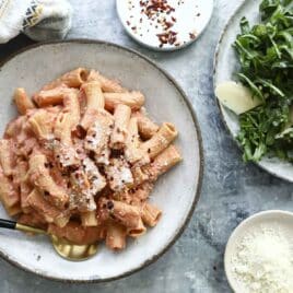 Penne alla vodka on a gray plate next to a plate of arugula salad.