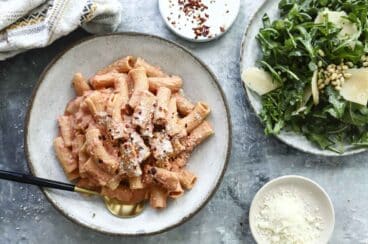 Penne alla vodka on a gray plate next to a plate of arugula salad.
