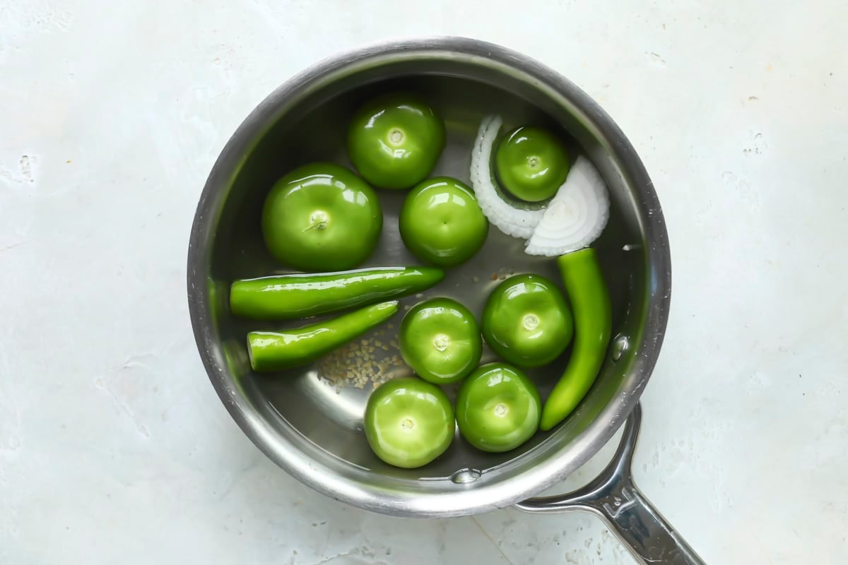 Tomatillos, serranos, onions, and garlic in a pot with water to boil for salsa verde.