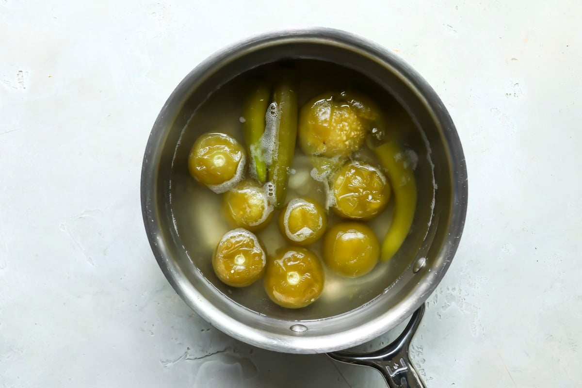 Boiled tomatillos, serranos, onions, and garlic in a pot with water for salsa verde.