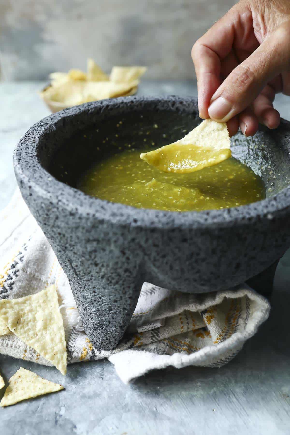 Someone dipping a chip into a molcajete with salsa verde inside.