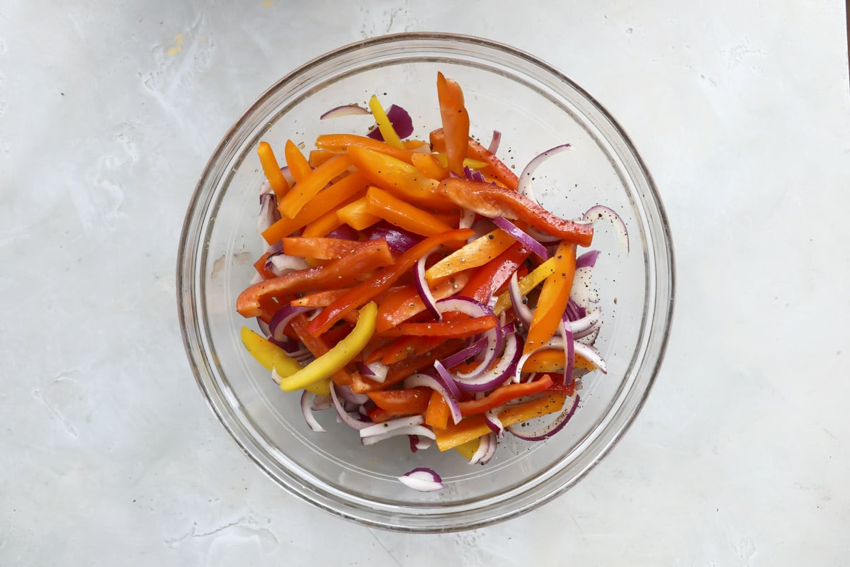 Seasoned bell peppers and onions in a glass bowl.