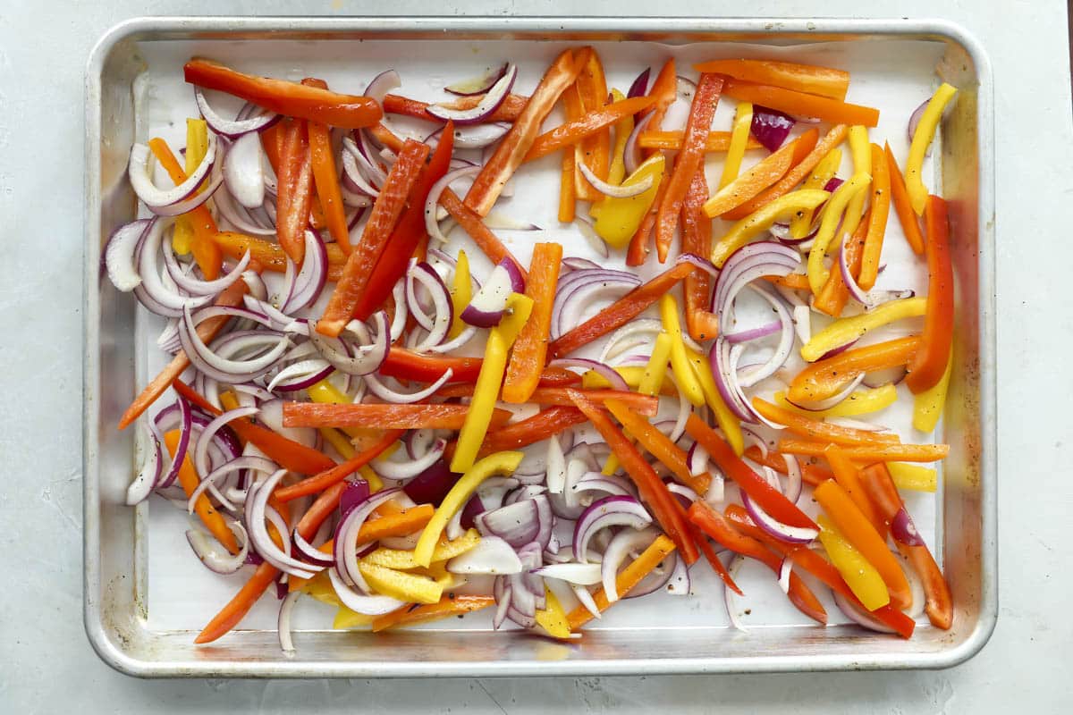 Seasoned bell peppers and onions on a baking sheet.