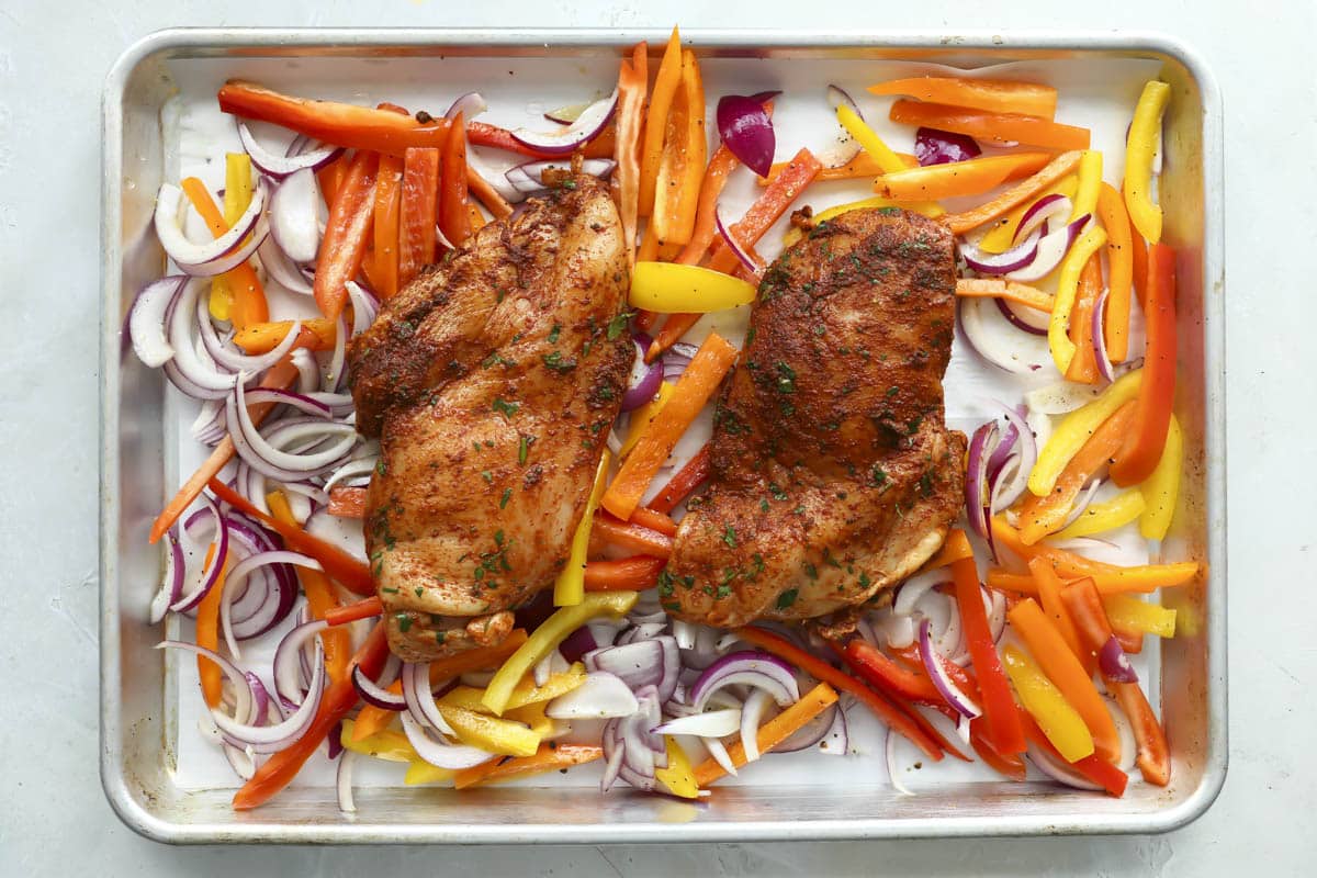 Sheet pan chicken fajitas on a baking sheet before cooking.