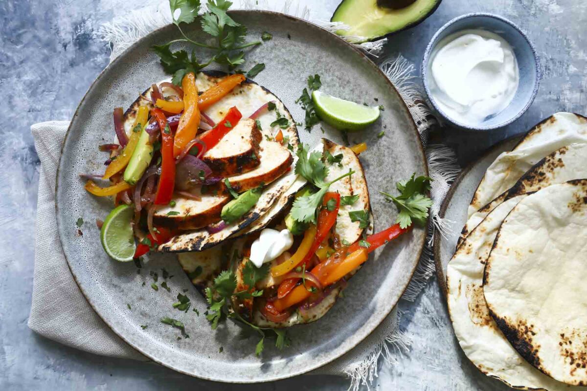A plate of chicken fajitas with sliced chicken breast, peppers, onions, and lime wedges.