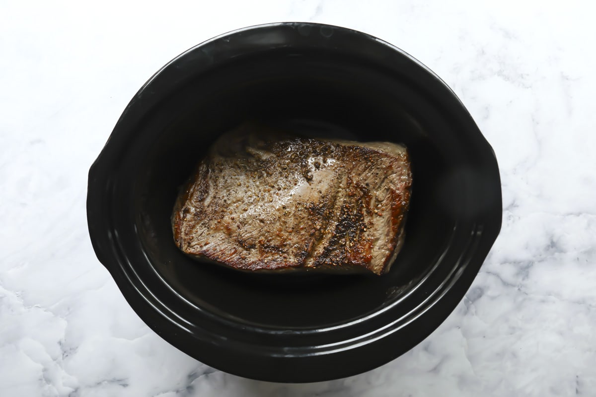 A cooked beef brisket in a slow cooker.
