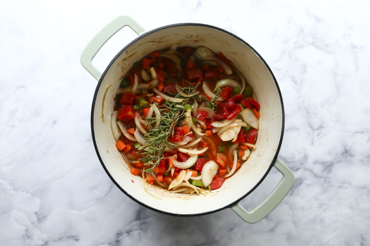 Onions, carrots, tomatoes, herbs, and celery cooking in a Dutch oven.