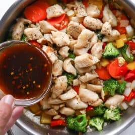 Someone pouring stir fry sauce into a skillet of chicken and veggies.