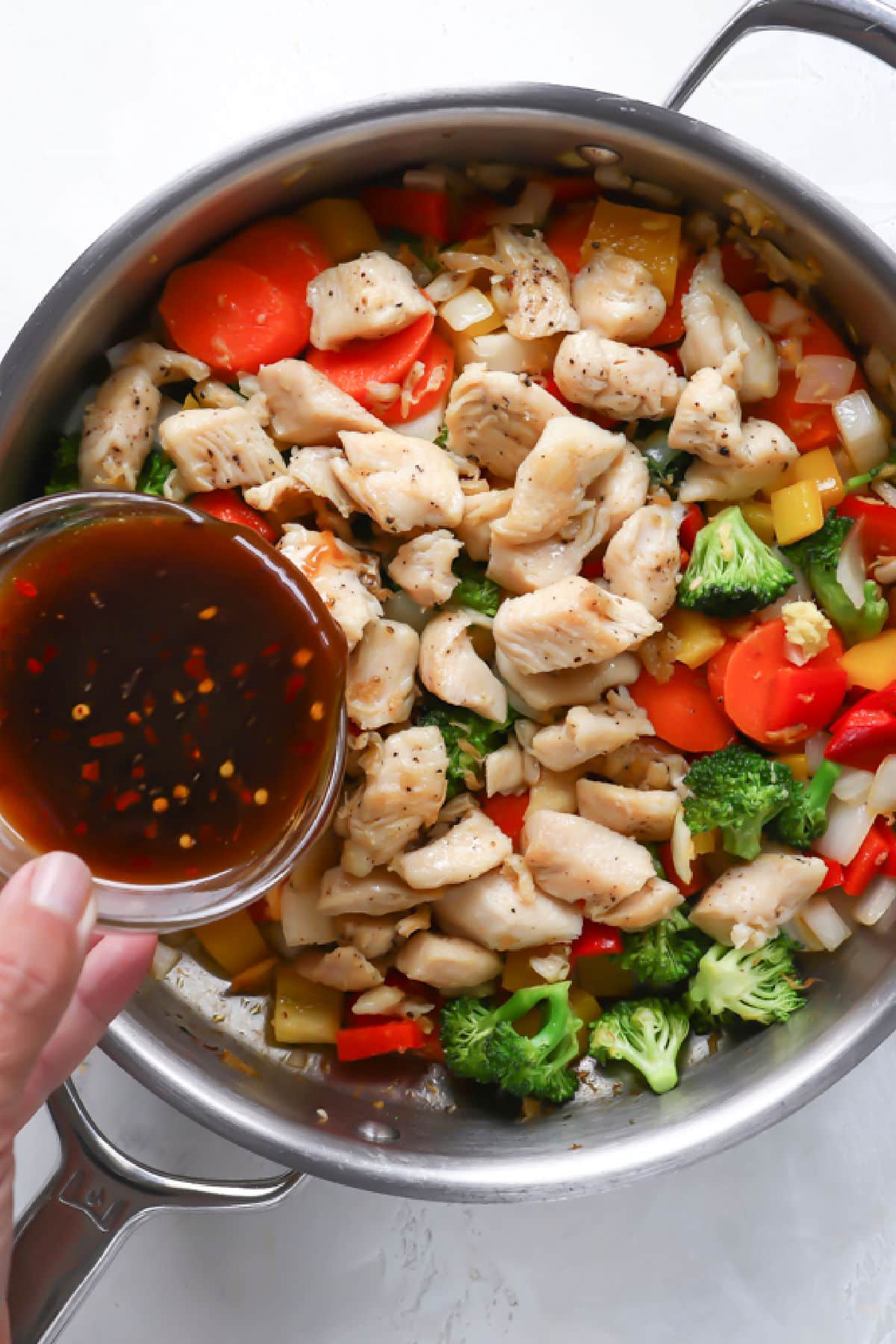 Someone pouring stir fry sauce into a skillet of chicken and veggies.
