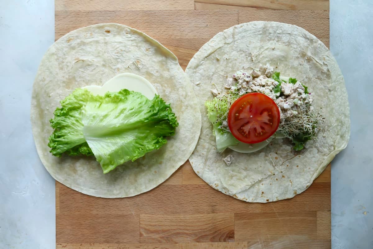 Two tuna wrap being assembled on a wooden cutting board.