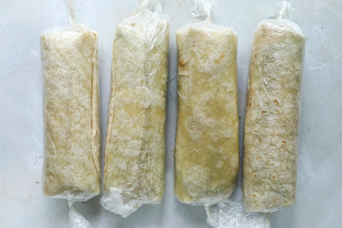 Four tuna wraps before being cut wrapped in plastic wrap.