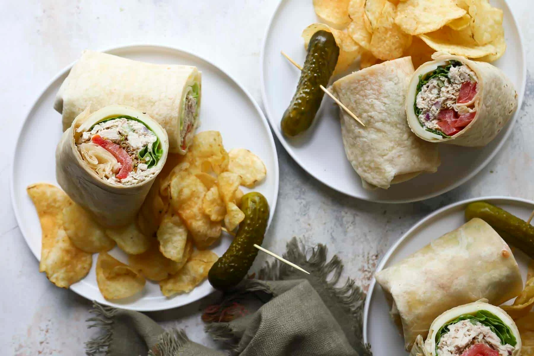 Three plates with tuna wraps, chips and a pickle.