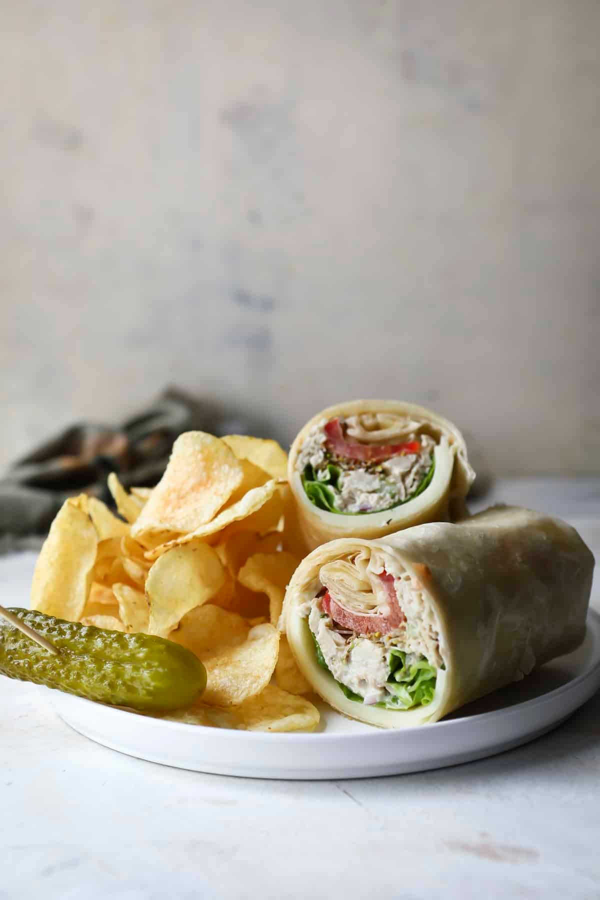 A tuna wrap on a plate with chips and a pickle.