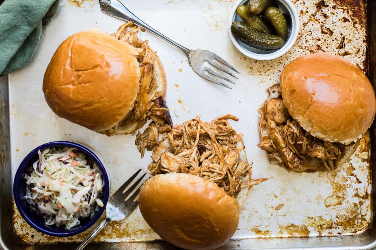 A metal tray with slow cooker pulled chicken sandwiches.