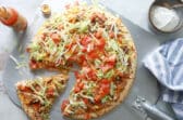 A taco pizza with a slice cut.