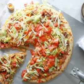 A taco pizza with a slice cut.