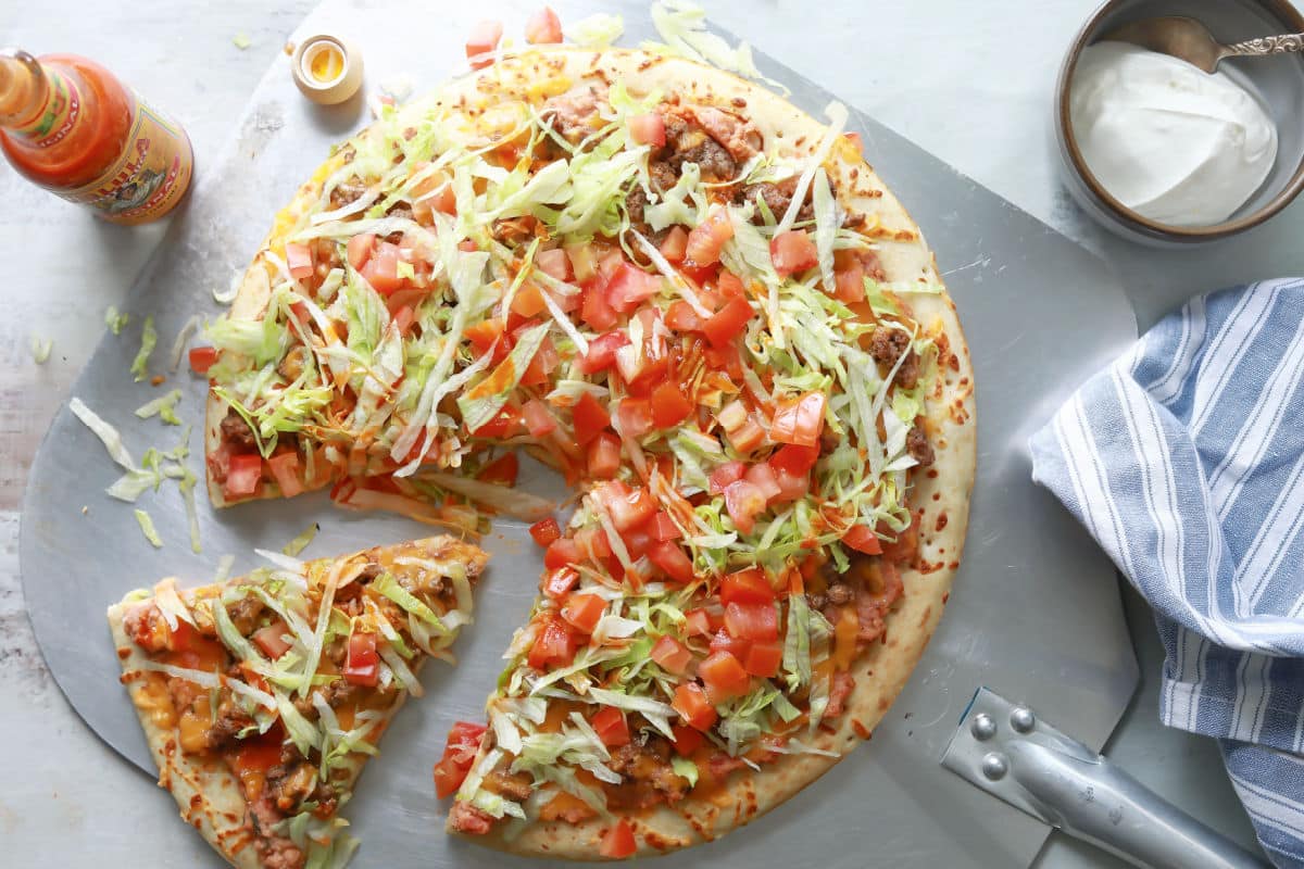 A taco pizza with a slice cut.