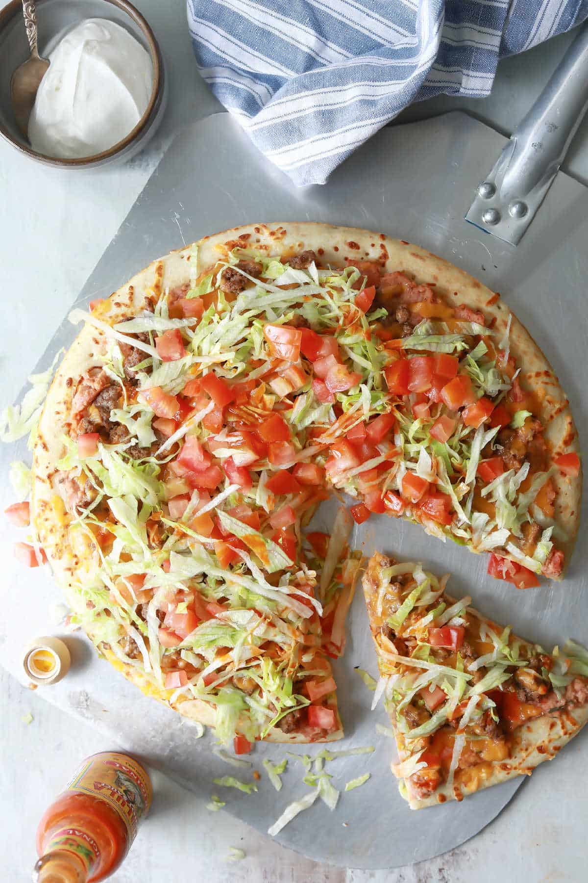 A taco pizza with a slice cut.