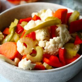 A bowl of Giardiniera next to a mason jar of Giardiniera.