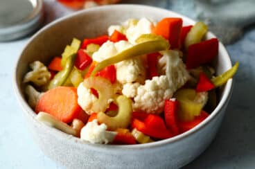 A bowl of Giardiniera next to a mason jar of Giardiniera.
