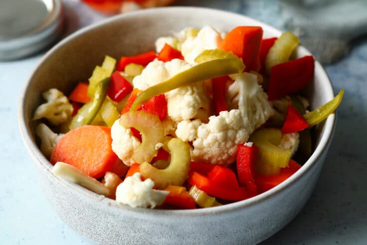 A bowl of Giardiniera next to a mason jar of Giardiniera.