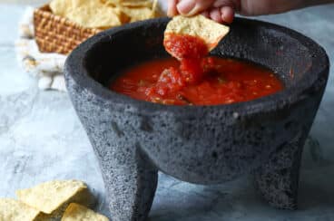 A molcajete with salsa ranchera and someone dipping a chip.