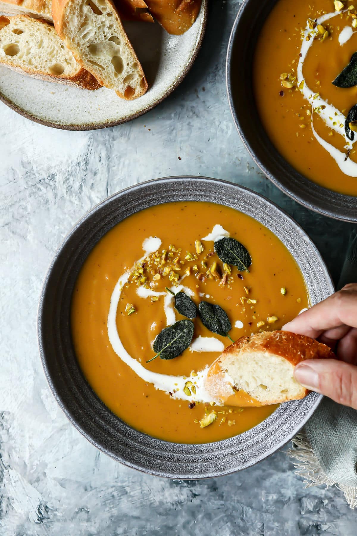 A bowl of butternut squash soup with someone dipping bread into it.
