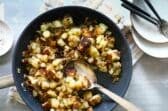 A skillet of home fries with a wooden spoon.