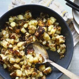 A skillet of home fries with a wooden spoon.