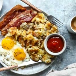 A plate of sunny-side up eggs, hashbrowns, bacon and ketchup.