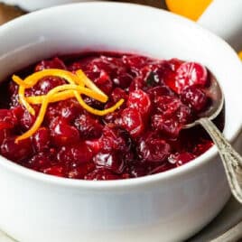 A bowl of cranberry sauce with some curls of orange zest on top.