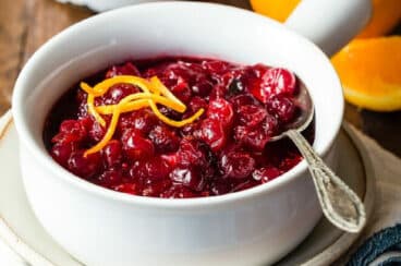 A bowl of cranberry sauce with some curls of orange zest on top.