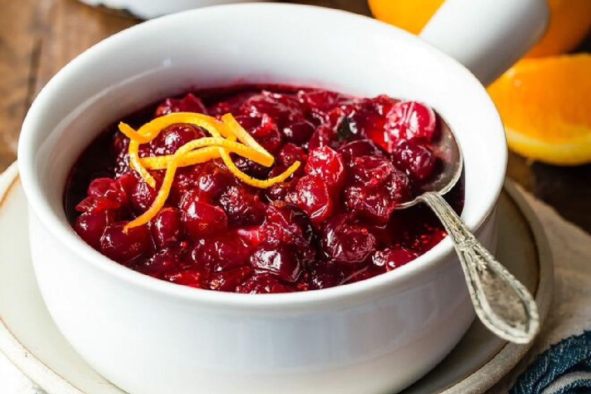 A bowl of cranberry sauce with some curls of orange zest on top.