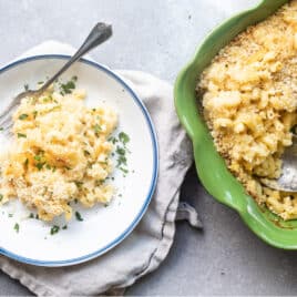 A plate of mac and cheese next to a green casserole dish.