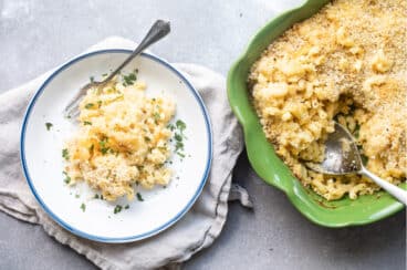 A plate of mac and cheese next to a green casserole dish.