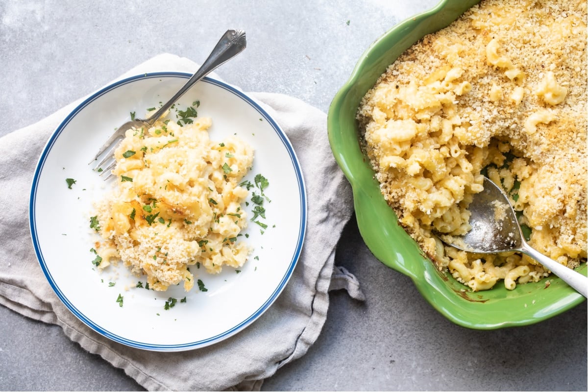 A plate of mac and cheese next to a green casserole dish.