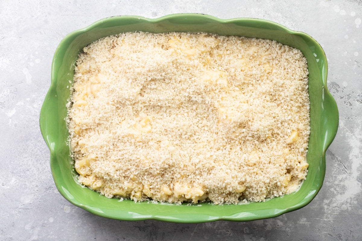 A green casserole dish full of mac and cheese with bread crumbs on top.