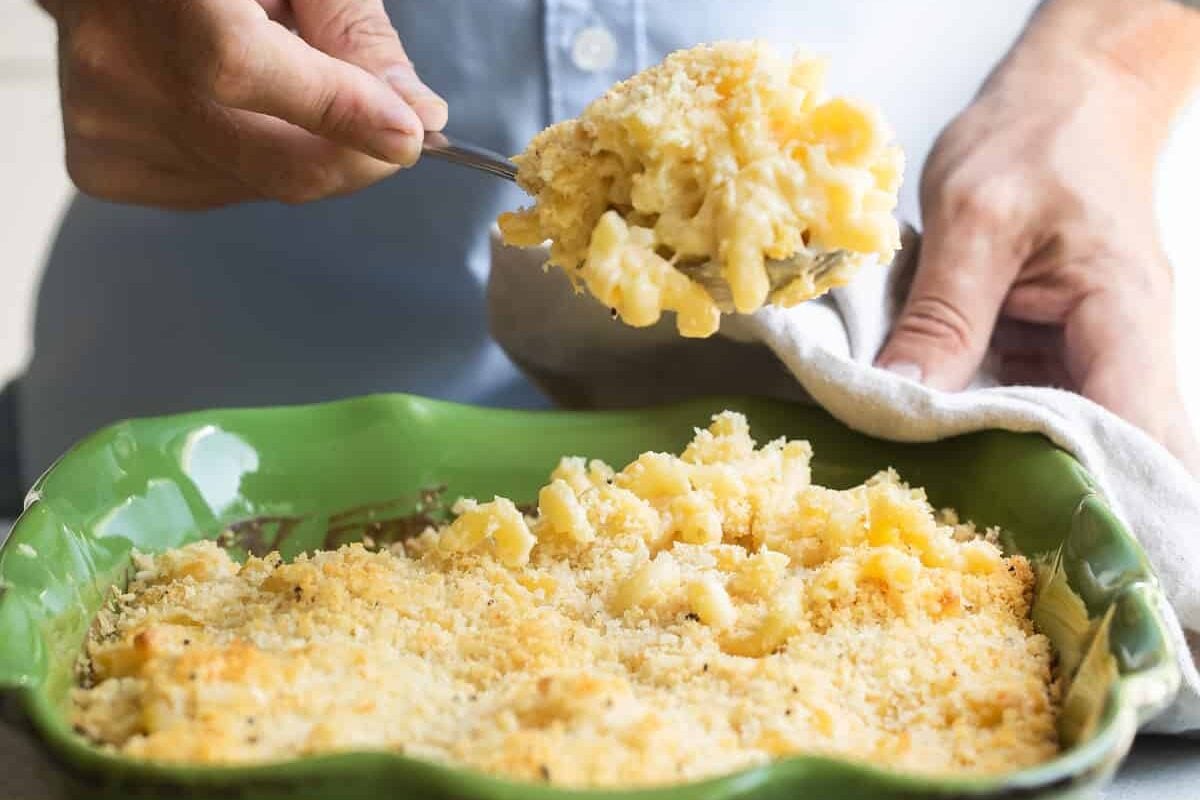 Someone scooping mac and cheese out of a green casserole dish.