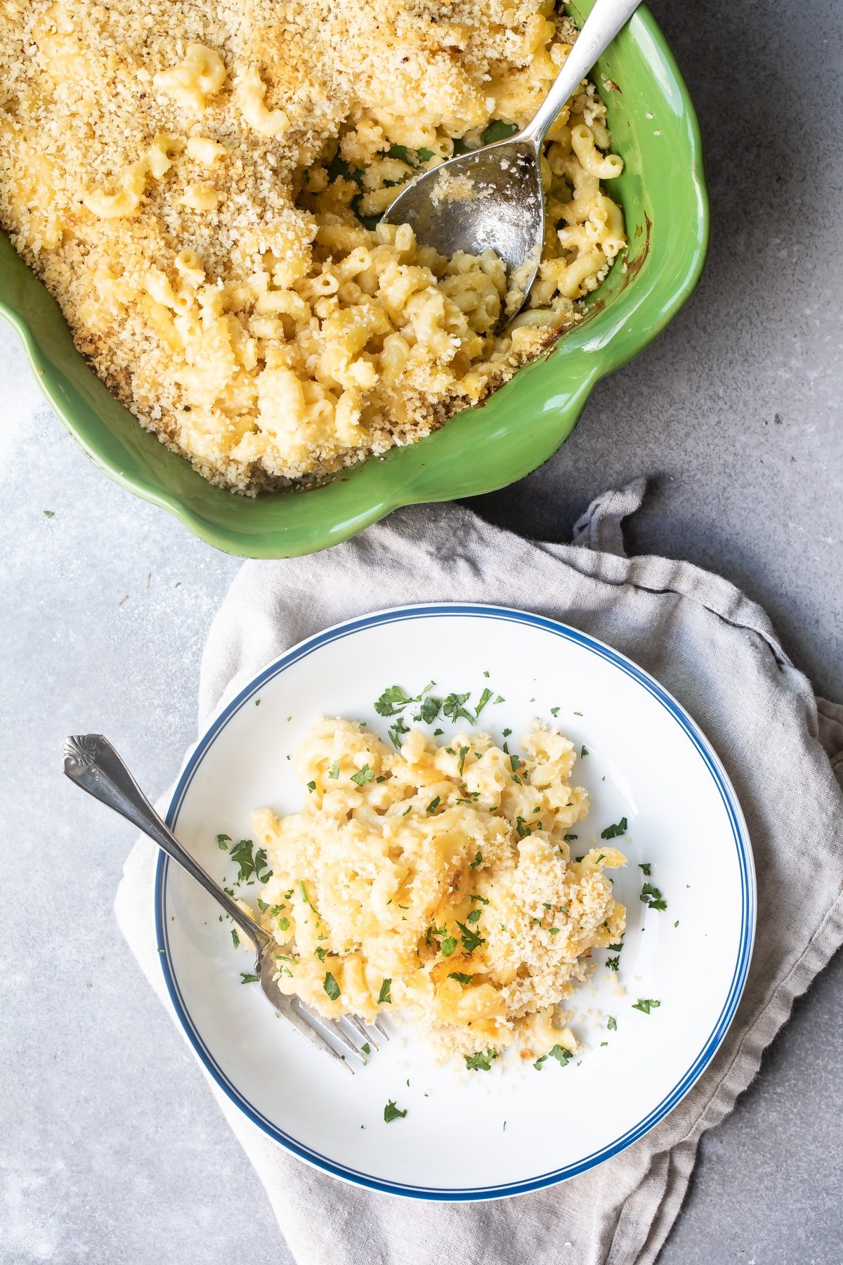 A plate of mac and cheese next to a green casserole dish.